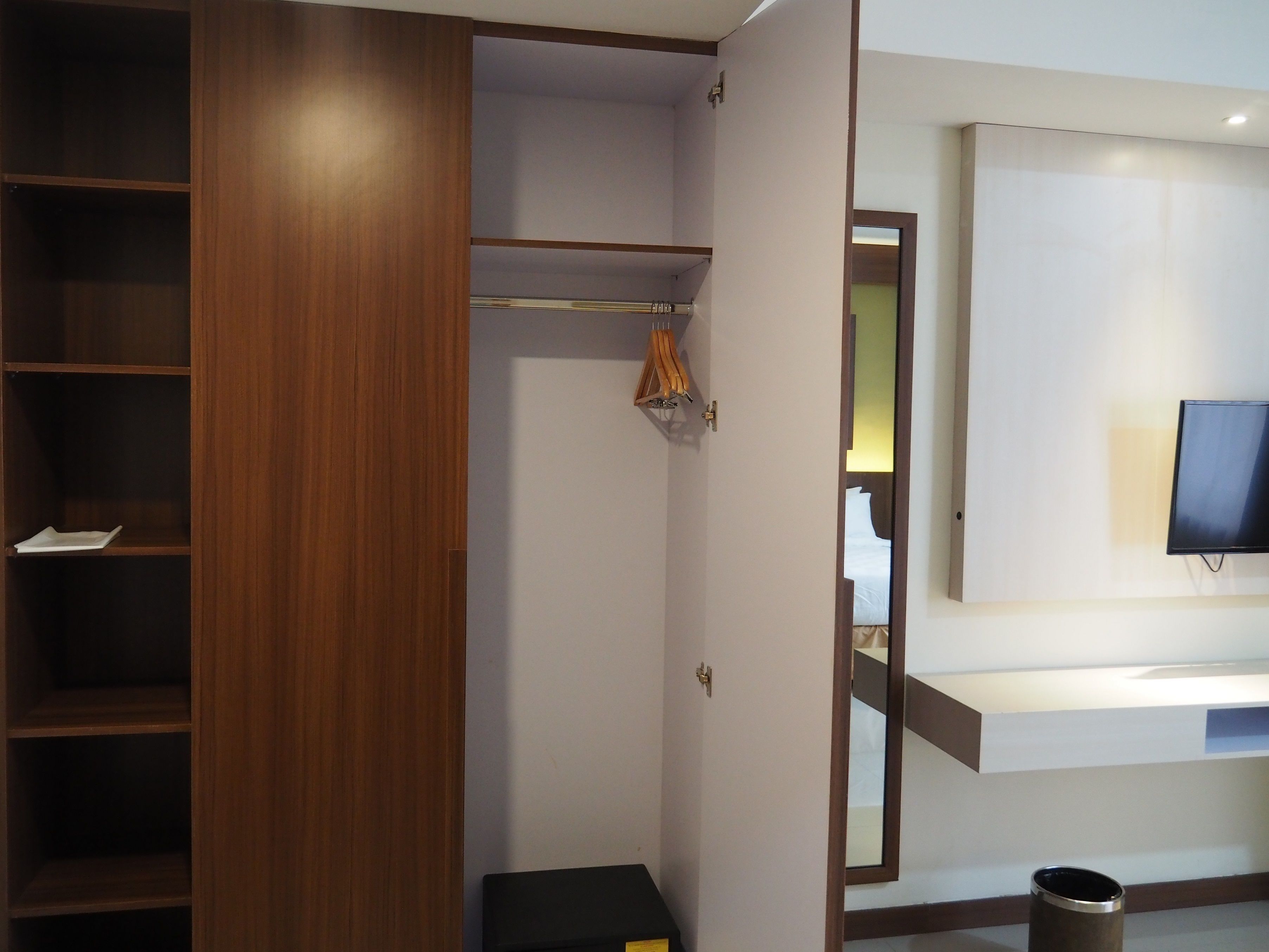 Habitación de hotel con un armario de madera, un televisor de pantalla plana en la pared y un pequeño cubo de basura.