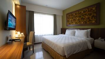 A hotel room with a bed, a desk with a chair, a television, and a painting on the wall.