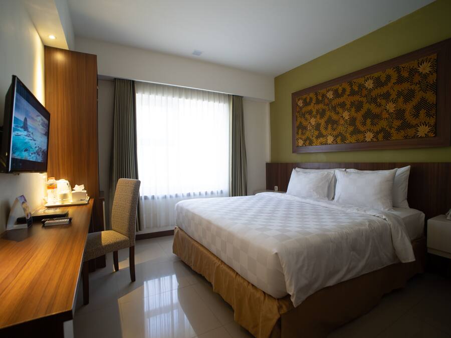 A hotel room with a bed, a desk with a chair, a television, and a painting on the wall.
