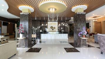 A modern hotel lobby with a reception desk, two large pillars, a chandelier, and a check-in counter.