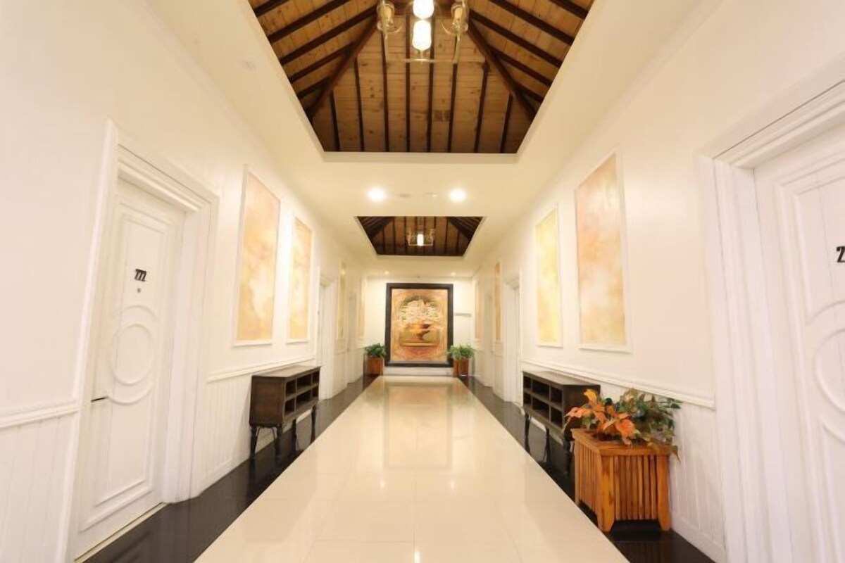 A hotel hallway with a polished floor, wooden ceiling beams, white walls, and framed artwork.