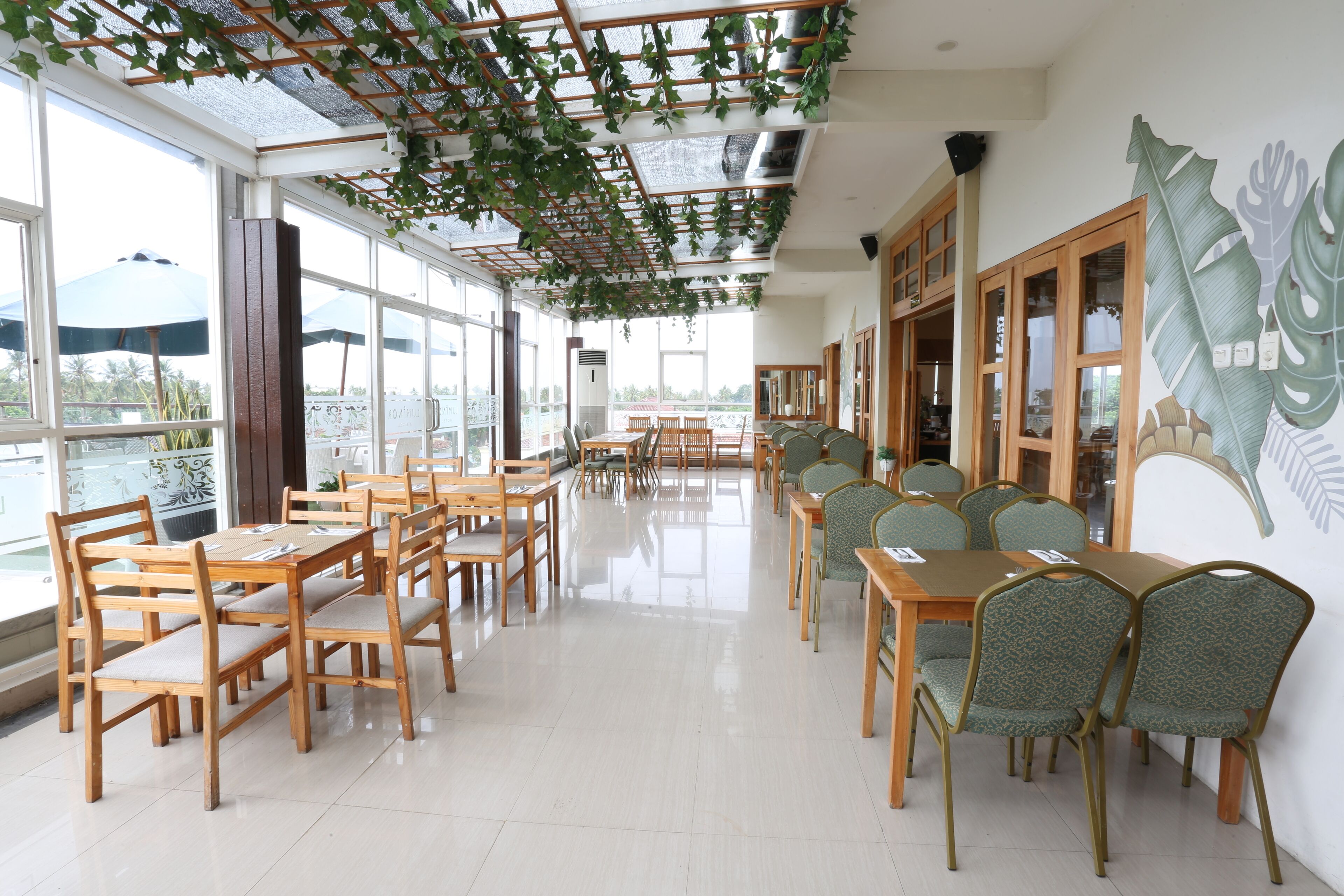 Een restaurant met houten tafels en stoelen, grote ramen en een plafond met hangende planten.