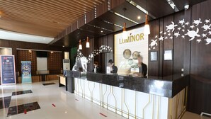 A reception area with a modern design, featuring a counter with a glass top and gold accents, a wooden ceiling, and a wall with a turtle mural. - Luminor Hotel Banyuwangi Yos Sudarso by WH (Banyuwangi)