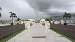 A pathway leading to a building with a glass pyramid structure, surrounded by white walls and palm trees. - Luminor Hotel Banyuwangi Yos Sudarso by WH (Banyuwangi)