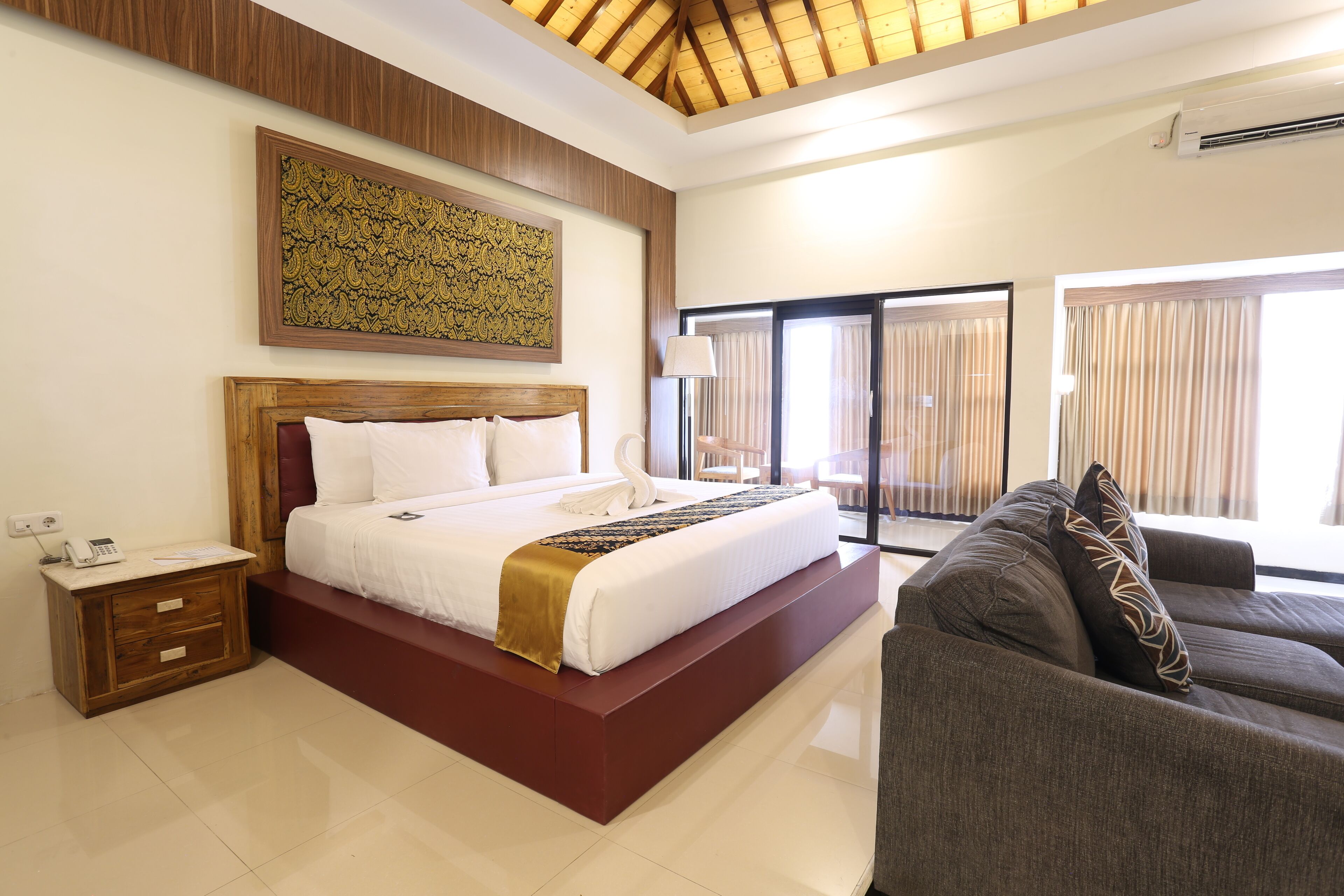 A modern bedroom with a large bed, a wooden headboard, a bedside table with a phone, and a large window with curtains.