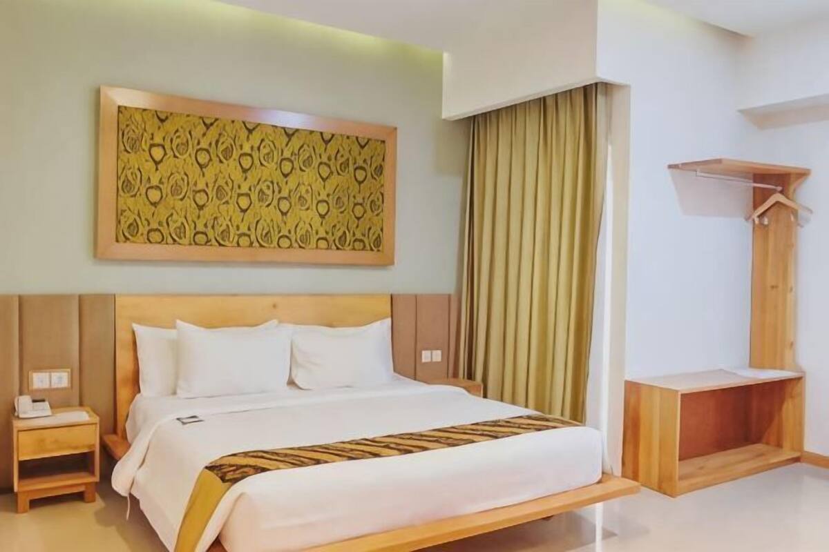Une chambre d’hôtel comprenant un lit, une table de chevet, un banc en bois, un porte-manteau et une décoration murale à motifs.