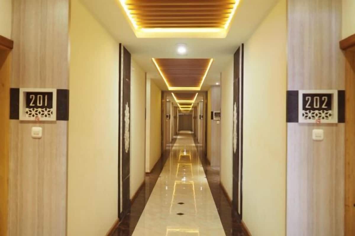 A long, narrow hotel corridor with wooden paneling on the walls, numbered doors, and a reflective floor.