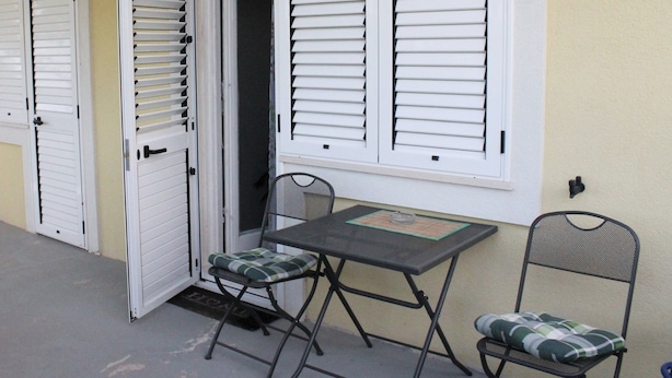 Uma pequena área externa com mesa e duas cadeiras, uma porta e uma janela com persianas.