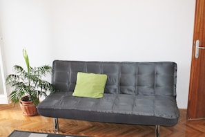 A grey sofa with a green pillow in a room with wooden flooring and a potted plant. - Apartment Bile (Kastela)
