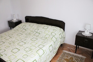 A bedroom with a bed, two bedside tables, a nightstand, a lamp, and a patterned rug. - Apartment Bile (Kastela)