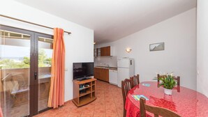 En balkong med en skjutdörr, en tv, en liten köksdel och ett matbord med stolar.
