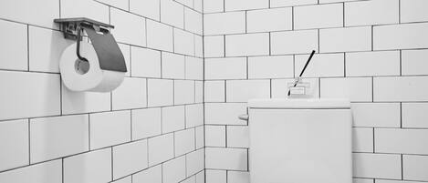 A small, white-tiled bathroom with a toilet and a paper towel dispenser mounted on the wall.
