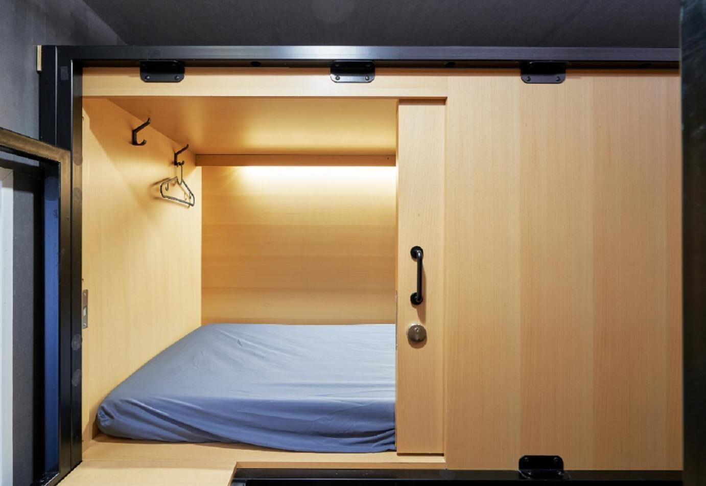 A compact room with a single bed, a wooden wardrobe, and a small hanging rack.