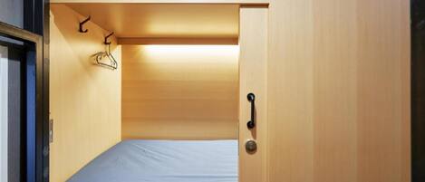 A compact room with a single bed, a wooden wardrobe, and a small hanging rack.