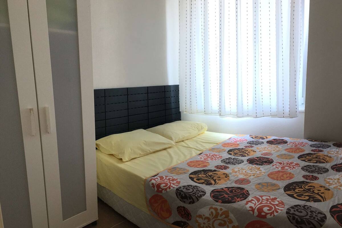 A bedroom with a bed, a window with curtains, and a wardrobe.