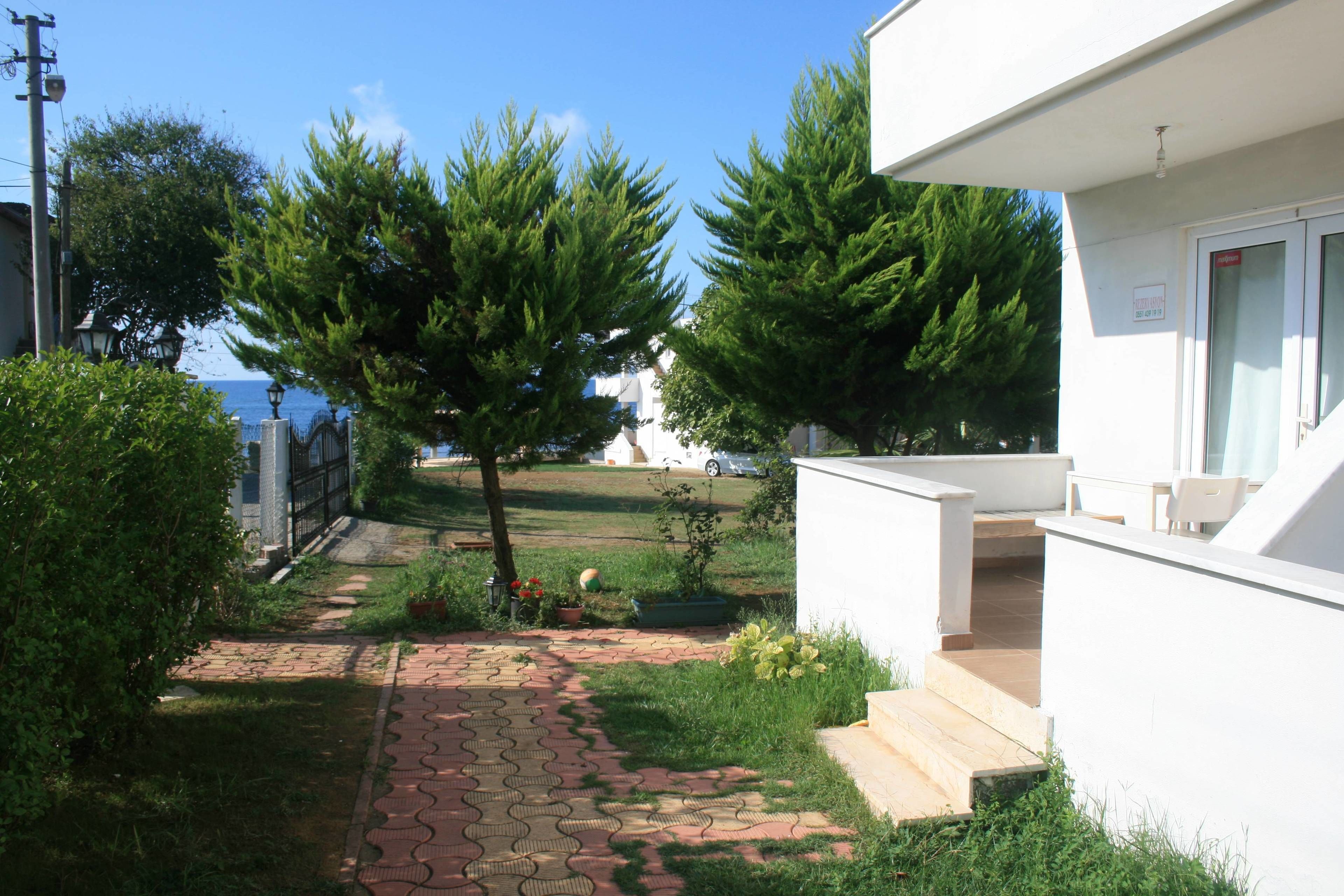 Un sendero conduce a un edificio blanco con un pequeño jardín, un árbol y vistas al mar.