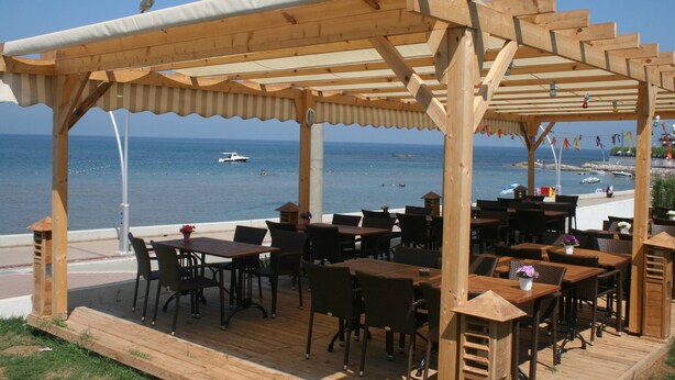An outdoor wooden deck with tables and chairs, overlooking a body of water with boats. - Ergul Apart Hotel (Kandira)