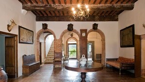Un vaste hall doté d’un plafond haut, de poutres apparentes en bois et d’une table ronde centrale sur laquelle sont posées une horloge et des théières.