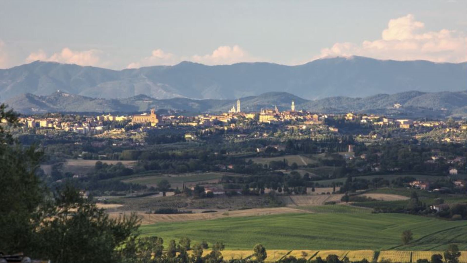 A town with a prominent church and several towers, surrounded by mountains and green fields.