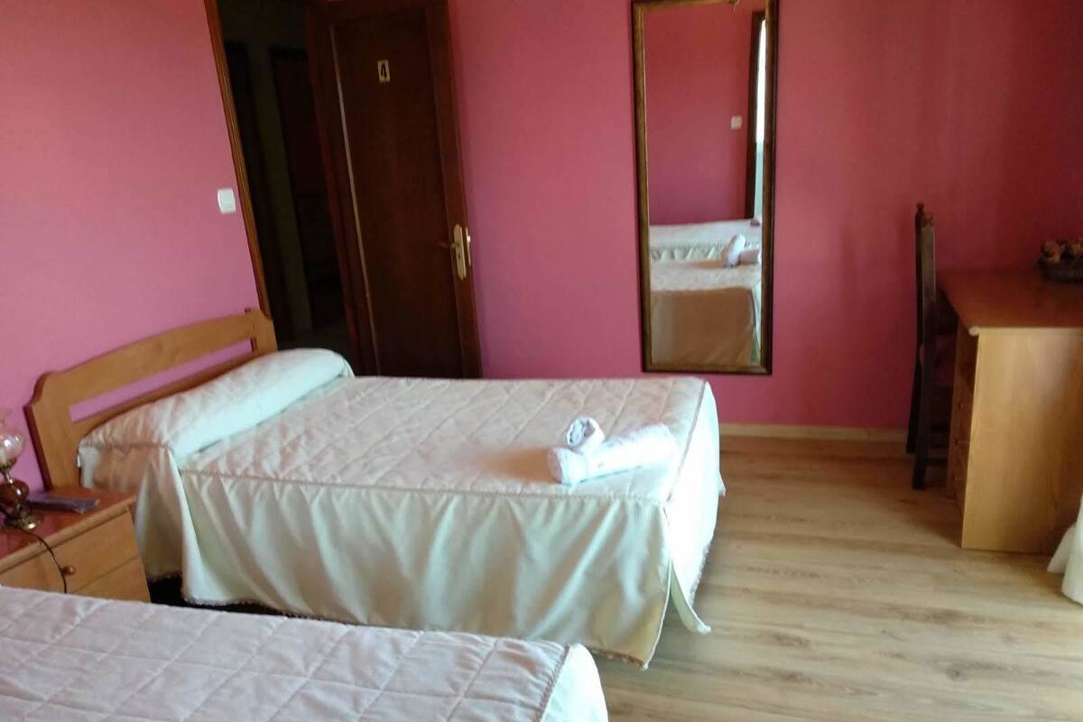 Habitación de hotel con dos camas, cabecero y cómoda de madera, un espejo y una puerta con un número.