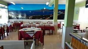 A restaurant with multiple tables, red tablecloths, and a mural of a coastal scene on the wall. - Hostal Cachiño (Carnota)