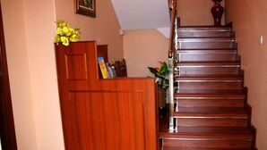 A wooden reception desk with a door, a staircase with wooden steps, and a vase with flowers on the landing. - Hostal Cachiño (Carnota)