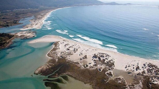 An aerial view of a coastal area with a sandy beach, clear blue waters, and a river flowing into the sea. - Hostal Cachiño (Carnota)