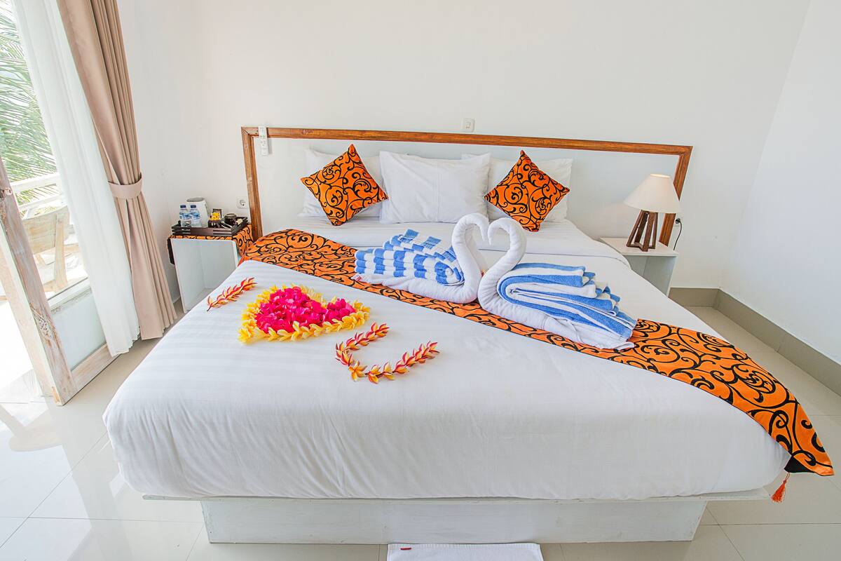 A neatly made bed with a heart-shaped floral arrangement, two swan-shaped towels, and a decorative headboard.