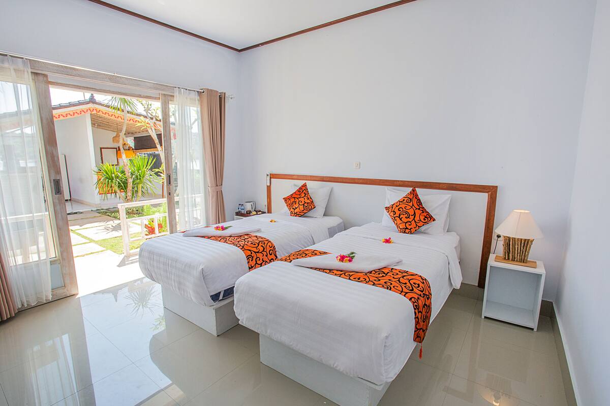A hotel room with two beds, a nightstand, and a view of a garden through the sliding glass door.