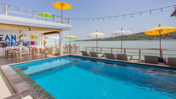 Zona de piscina con sillones reclinables y sombrillas, con vista a una masa de agua.
