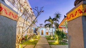Un sendero conduce a un edificio con una puerta, bordeado por palmeras y elementos decorativos.