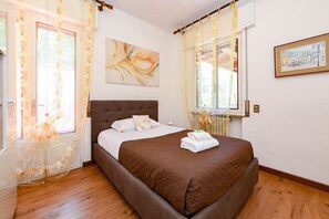 A bedroom with a bed, curtains, a painting, and a window.
