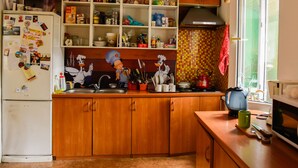 A kitchen with wooden cabinets, a refrigerator, a microwave, and a window with a view. - Almaty Hostel Dom (Almaty)