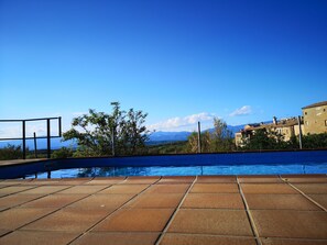 A swimming pool with tiled flooring, surrounded by trees and buildings, under a clear blue sky. - Casa Cal Fuster for 5 people (Pinell de Solsonès)