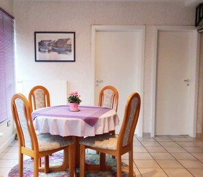 A dining area with a round table covered by a purple tablecloth, surrounded by wooden chairs with cushioned seats. A potted plant with pink flowers is placed on the table. - Ferienhaus & Nurdachhaus Rothaargebirge (Bad Berleburg)