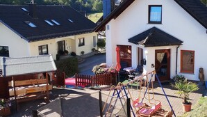 A residential area with a white house featuring a black roof, a wooden swing set, and a fenced yard. - Ferienhaus & Nurdachhaus Rothaargebirge (Bad Berleburg)