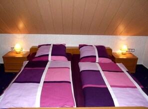 A double bed with a striped bedspread, two bedside tables with lamps, and a wooden ceiling. - Ferienhaus & Nurdachhaus Rothaargebirge (Bad Berleburg)