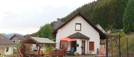A traditional chalet with a wooden porch, a red umbrella, and a trampoline in the yard.