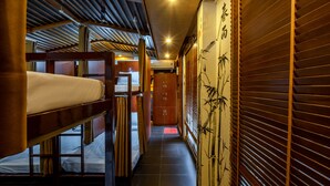 Un pasillo con literas, puertas de madera y una pared decorada con arte de bambú.