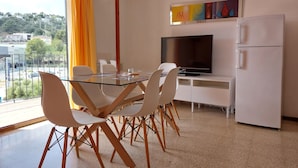 Eine moderne Küche mit einem Glastisch, weißen Stühlen, einem Flachbildfernseher und einem weißen Kühlschrank.