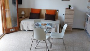 Ein Zimmer mit einem Bett, einem Tisch mit Stühlen, einem Deckenventilator, einem Fernseher und einem kleinen Schrank.