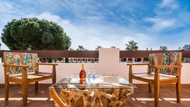 A terrace with a glass-top table, two wooden chairs with floral upholstery, and a bottle of wine. - Outstanding apart with pool view & terrace at Vila Sol (Quarteira)