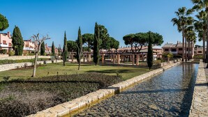 A serene courtyard with a stone-lined water feature, surrounded by neatly trimmed hedges and tall trees. - Outstanding apart with pool view & terrace at Vila Sol (Quarteira)