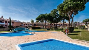 A swimming pool area with two pools, a bridge, and a row of buildings in the background. - Outstanding apart with pool view & terrace at Vila Sol (Quarteira)