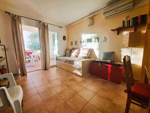 Sala de estar com sofá, uma mesa pequena, uma cadeira e uma porta de vidro deslizante que dá para uma área externa.