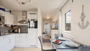 Una cocina moderna con armarios blancos, electrodomésticos de acero inoxidable y un comedor con una mesa para dos.
