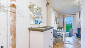Una habitación con puerta de madera, un espejo con luces, una mesa con sillas y vista a una casa afuera.