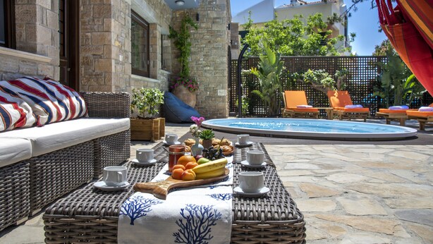Ein Patio mit Korbmöbeln, einem Esstisch mit Früchten, Tassen und einer Blumenvase.
