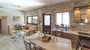 Eine moderne Küche mit Wandverkleidung aus Stein, ein Essbereich mit Glastisch und ein gemütliches Wohnzimmer mit Sofa und Couchtisch.