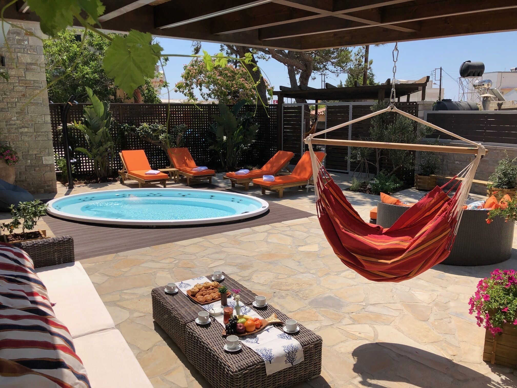 A poolside area with a hot tub, lounge chairs, a hanging hammock, and a table with snacks and drinks.